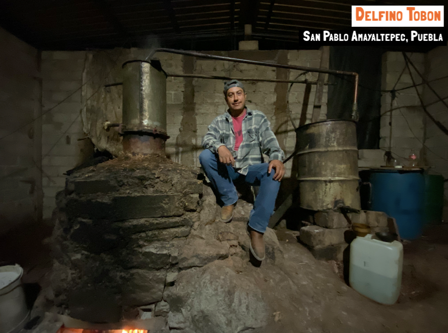 A man sat next to a copper pot still for mezcal