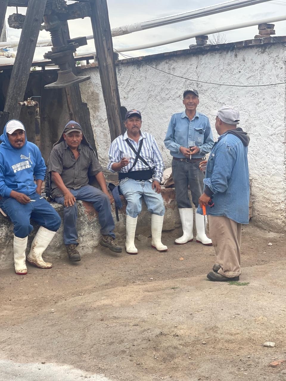 a group of men taking a break on a wall while working at a mezcal distillery