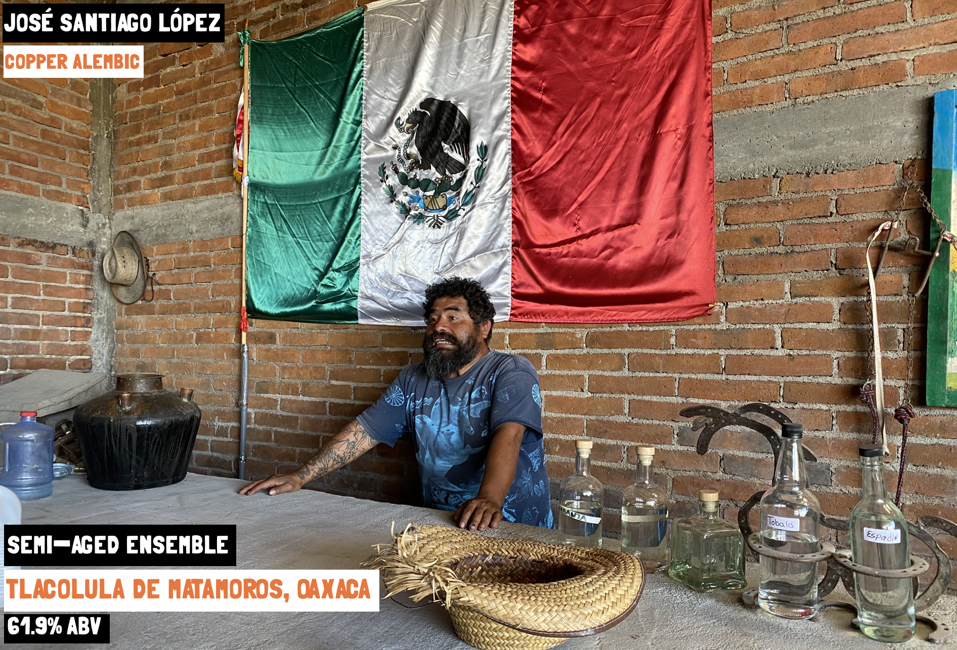 A man stood in front of the Mexican flag and next to bottles of mezcal