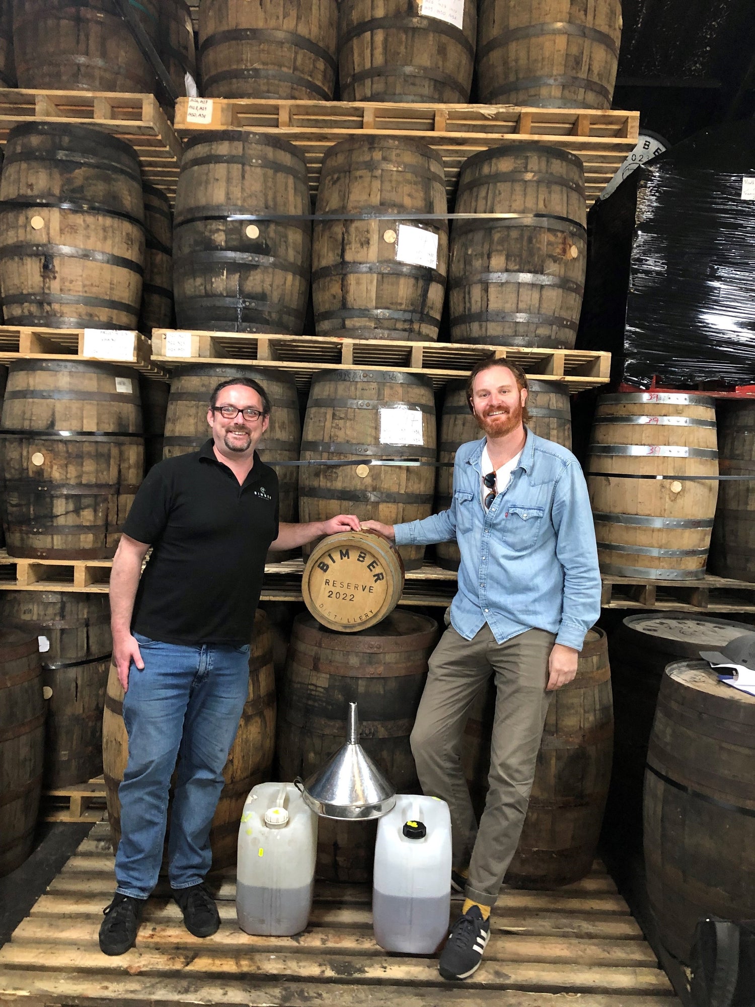 Jon Darby from the Sin Gusano Mezcal project stood with Matt from Bimber whiskey distillery in front of a wall of barrels ageing mezcal
