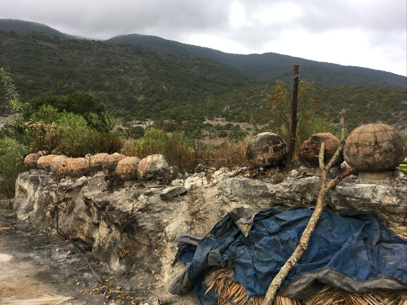 Clay mezcal pots sat on a wall with the Mexico landscape behind