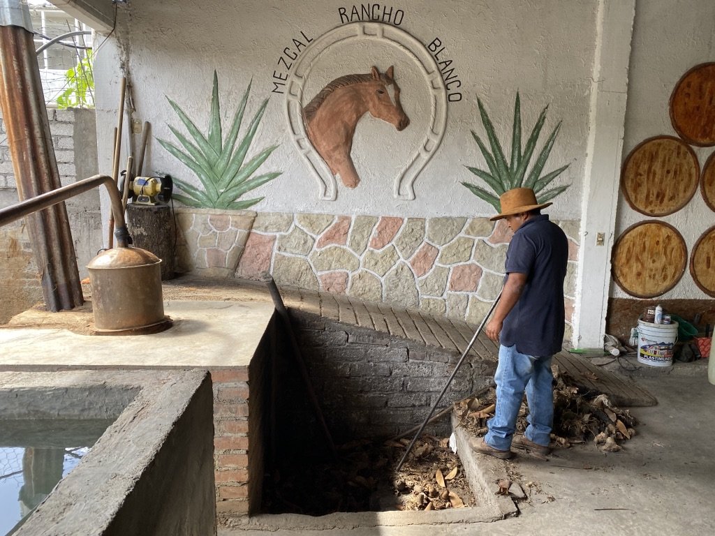 adding wood to a woodfire heating a copper pot still for mezcal