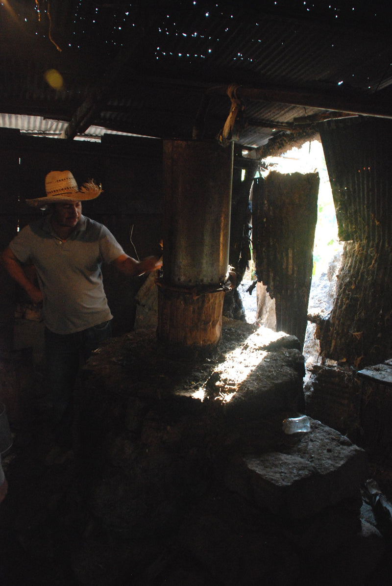A copper pot still making mezcal in a dark room 
