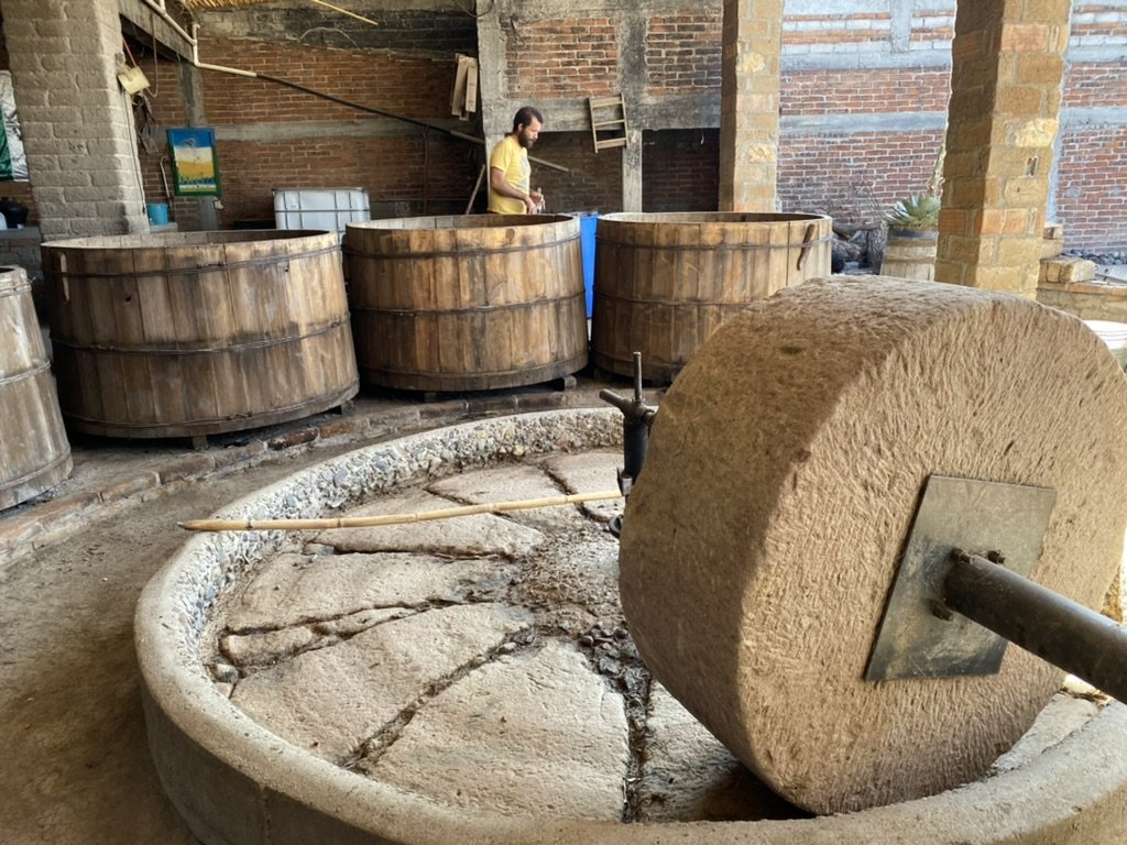 a stone tahona for milling and barrels for storing mezcal