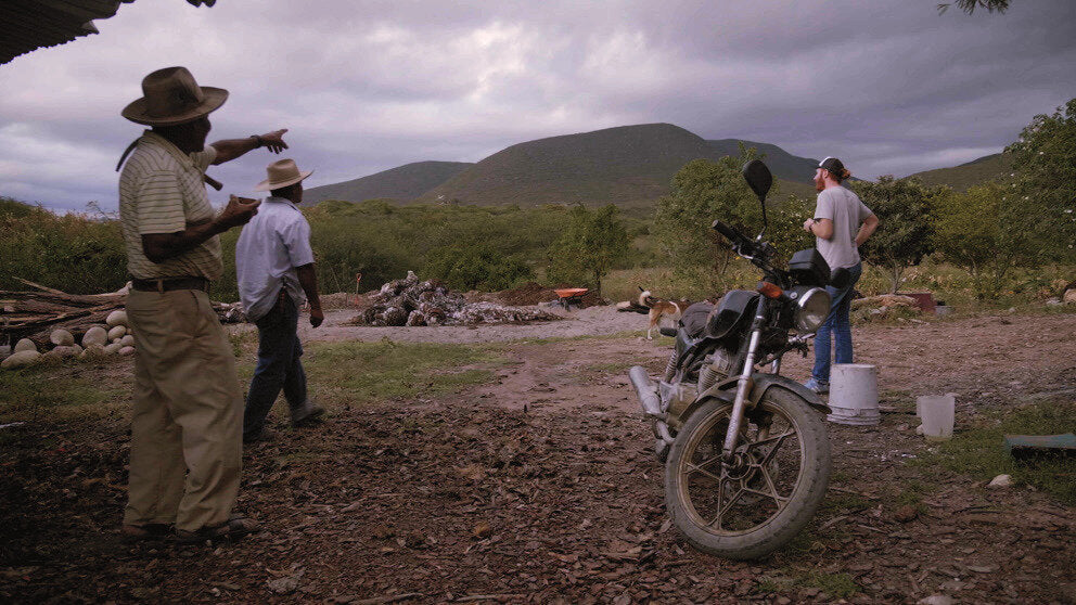 a group of men by a Motorcycle and outside oven used for cooking Pina's for mezcal