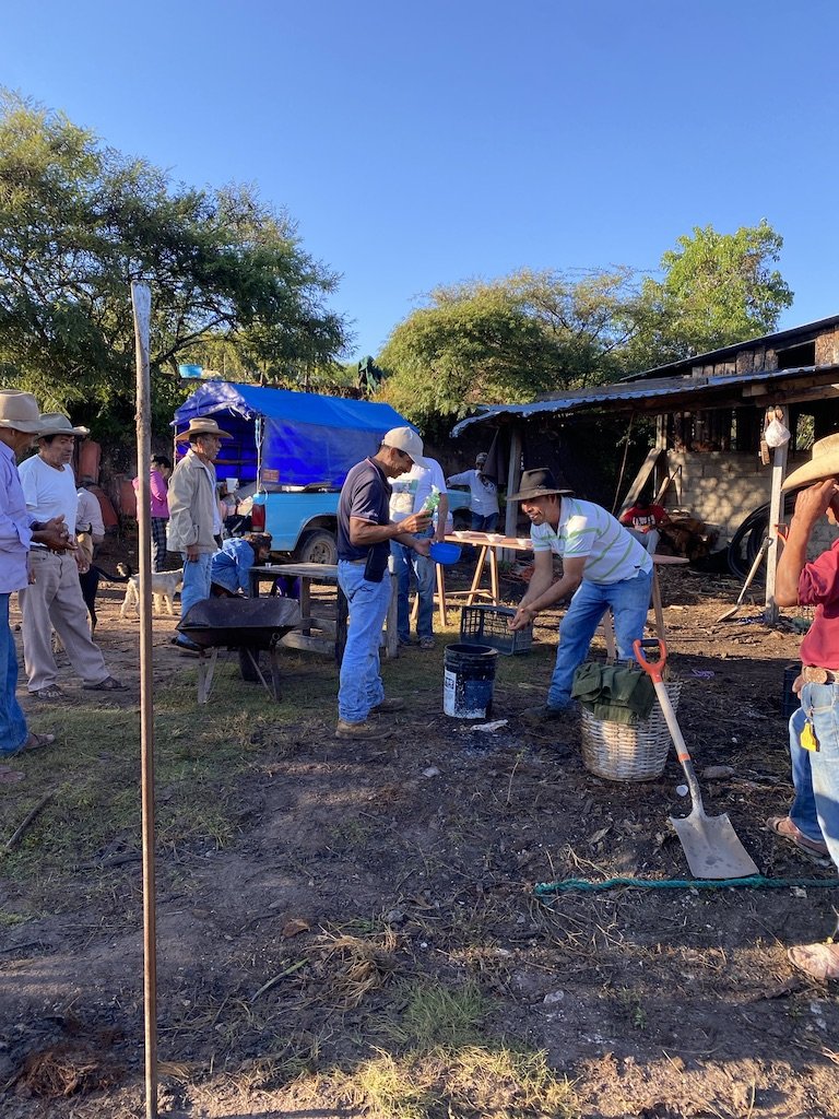 Group of people working outdoors with tools and equipment on a sunny day on a mezcal distillery 
