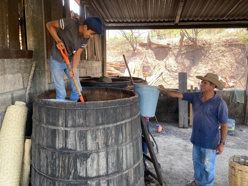 Two men working with large barrels in an outdoor setting to make Mezcal for the Sin Gusano project
