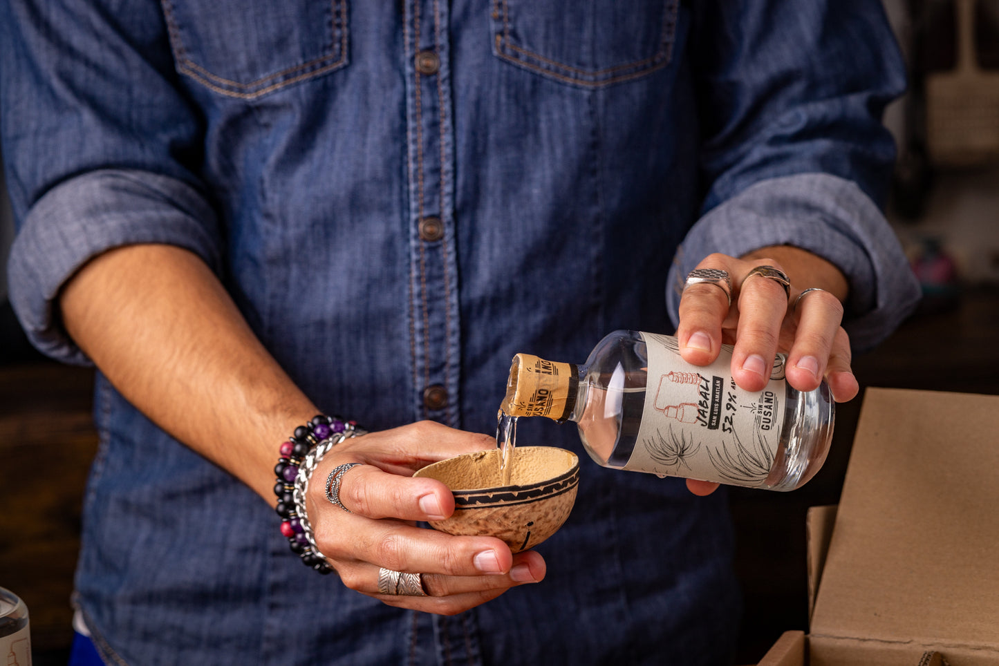 Person pouring mezcal from a bottle into a small bowl using a cork stopper.