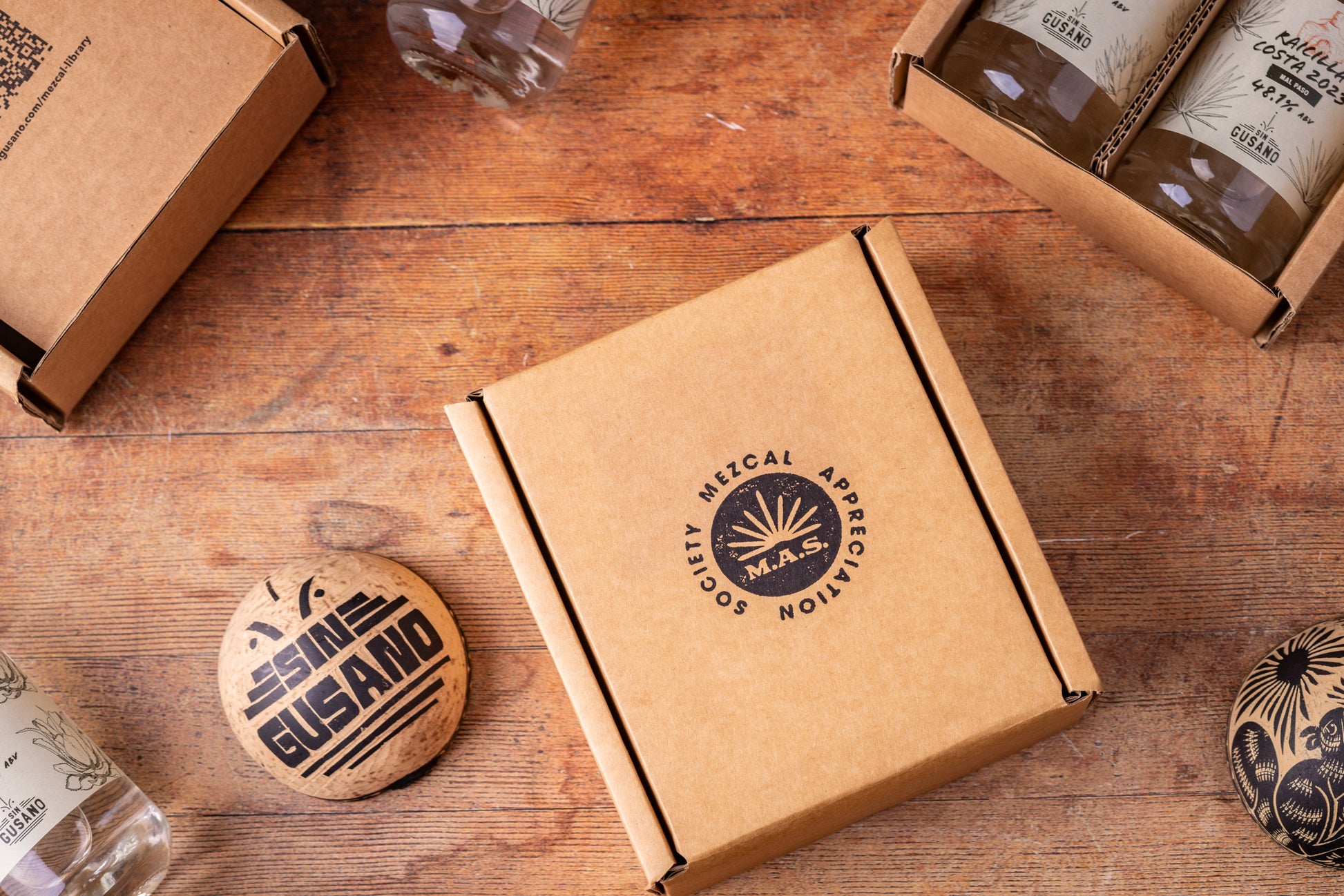 Mezcal packaging on a wooden surface with 'M.A.S.'(Mezcal Appreciation Society) branding.