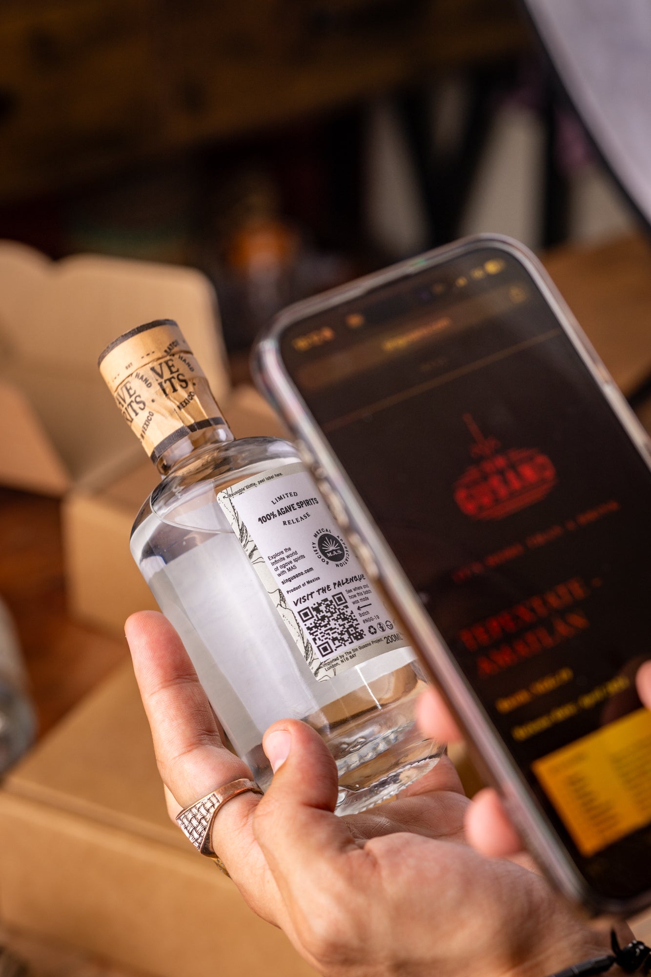 Person holding a bottle of mezcal and using a phone to scan the QR code opening the Sin Gusano Mezcal library.