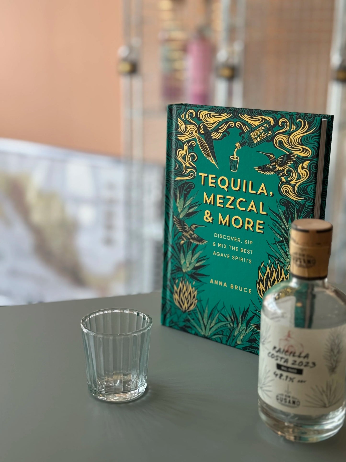 Tequila, Mezcal & More book with a bottle and shot glass on a table